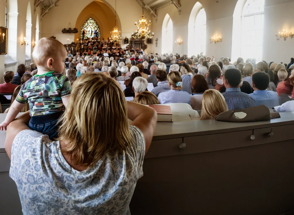 Mamma och hennes bebis i välfylld kyrka under en gudstjänst i Svenska kyrkan